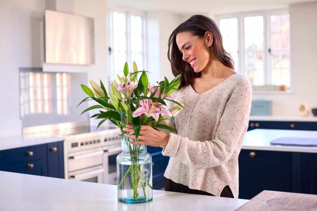 Smiling Woman At Home Arranging Bouquet Of Flowers In Glass Vase
