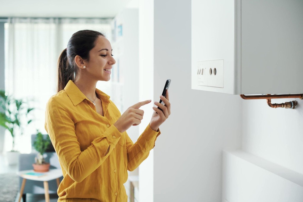 Woman managing and programming her water heater system using her smartphone, smart home concept